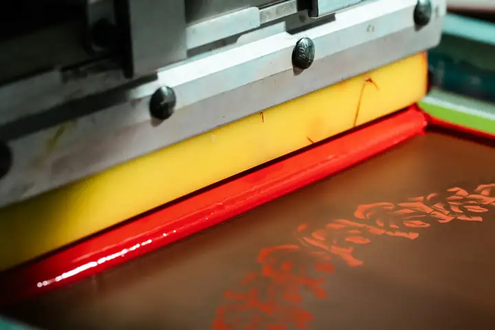 A squeegee pulling red ink across a silk screen.