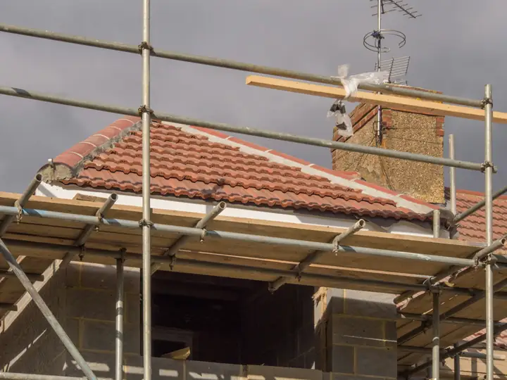 Scaffolding around the eaves of a house with a red tiled roof.